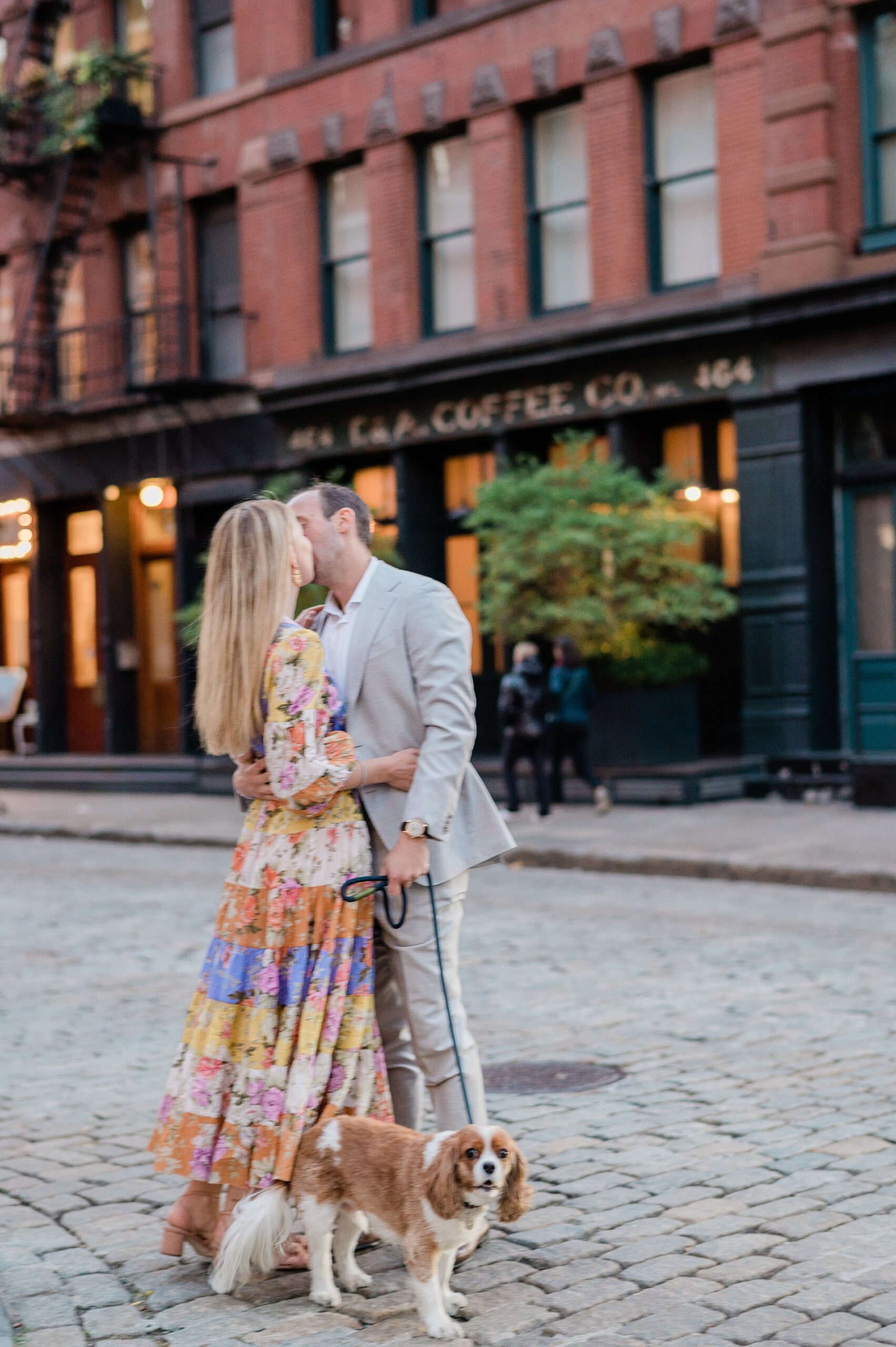 couple kiss while walking their dog during Summer Engagement in Tribeca NYC