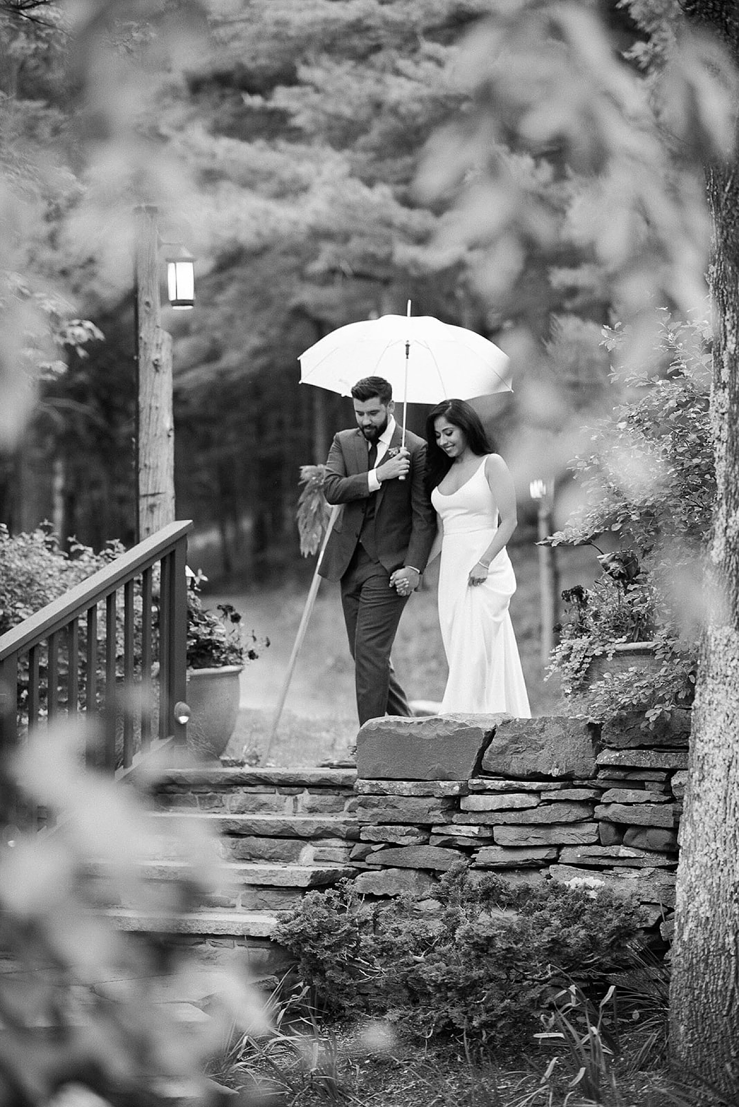 groom holds umbrella for bride during the rain