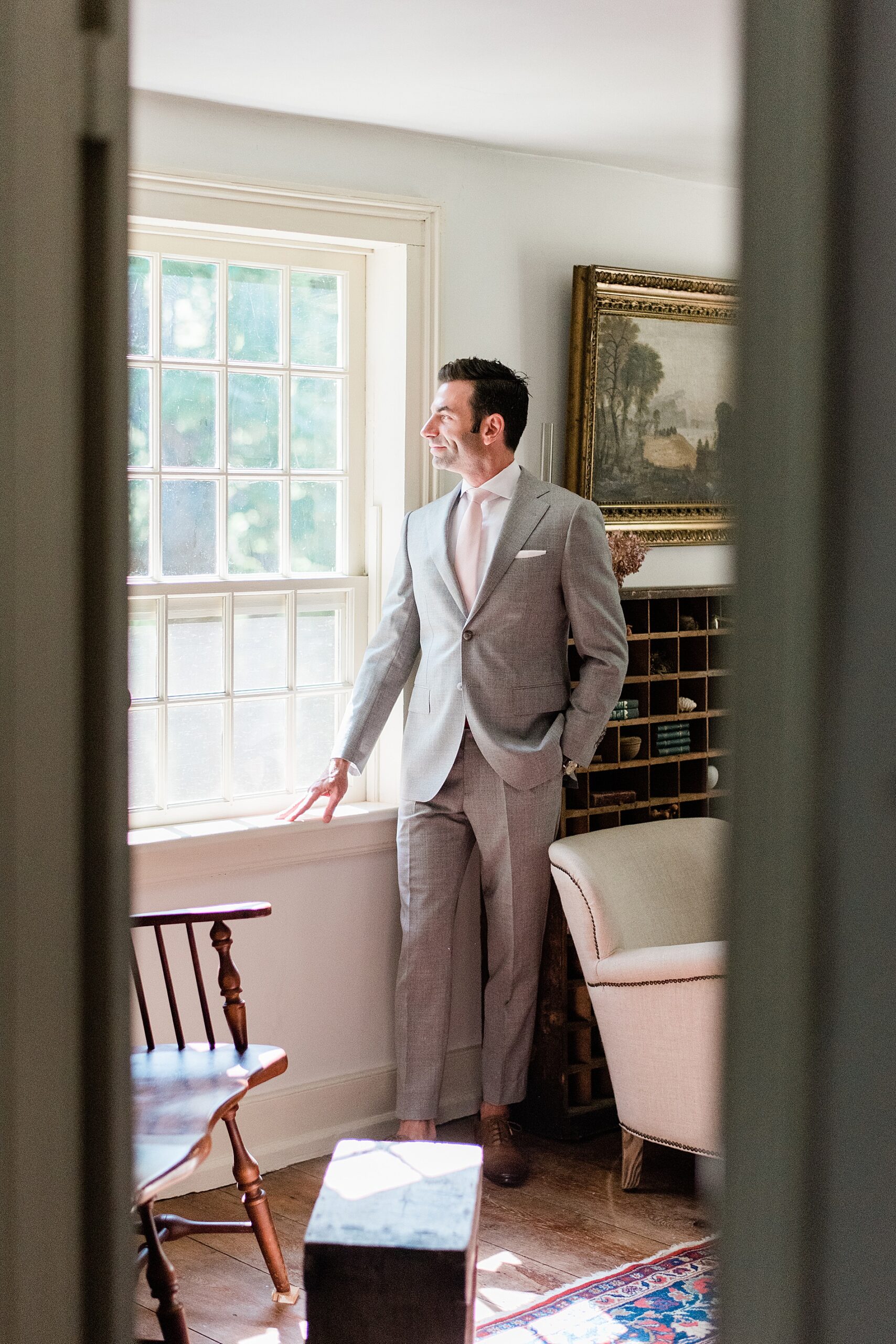 groom in gray suite looks out window
