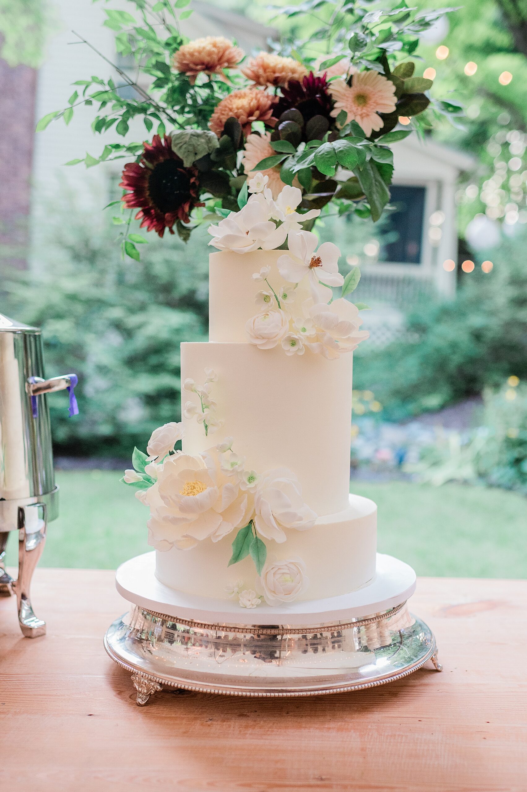three tiered wedding cake with white flowers and topped with maroon and light pink flowers