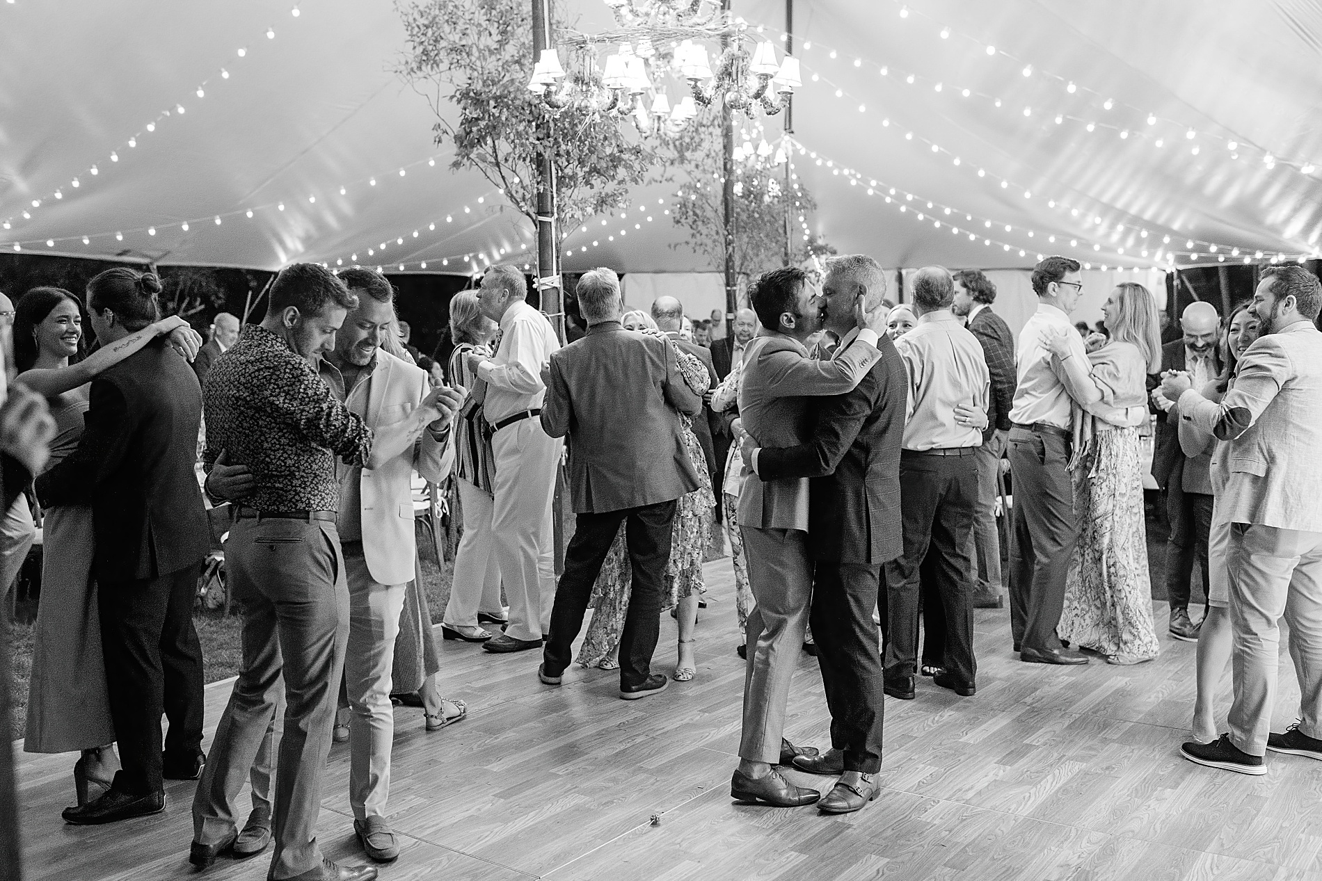 grooms kiss on the dance floor surrounded by guests