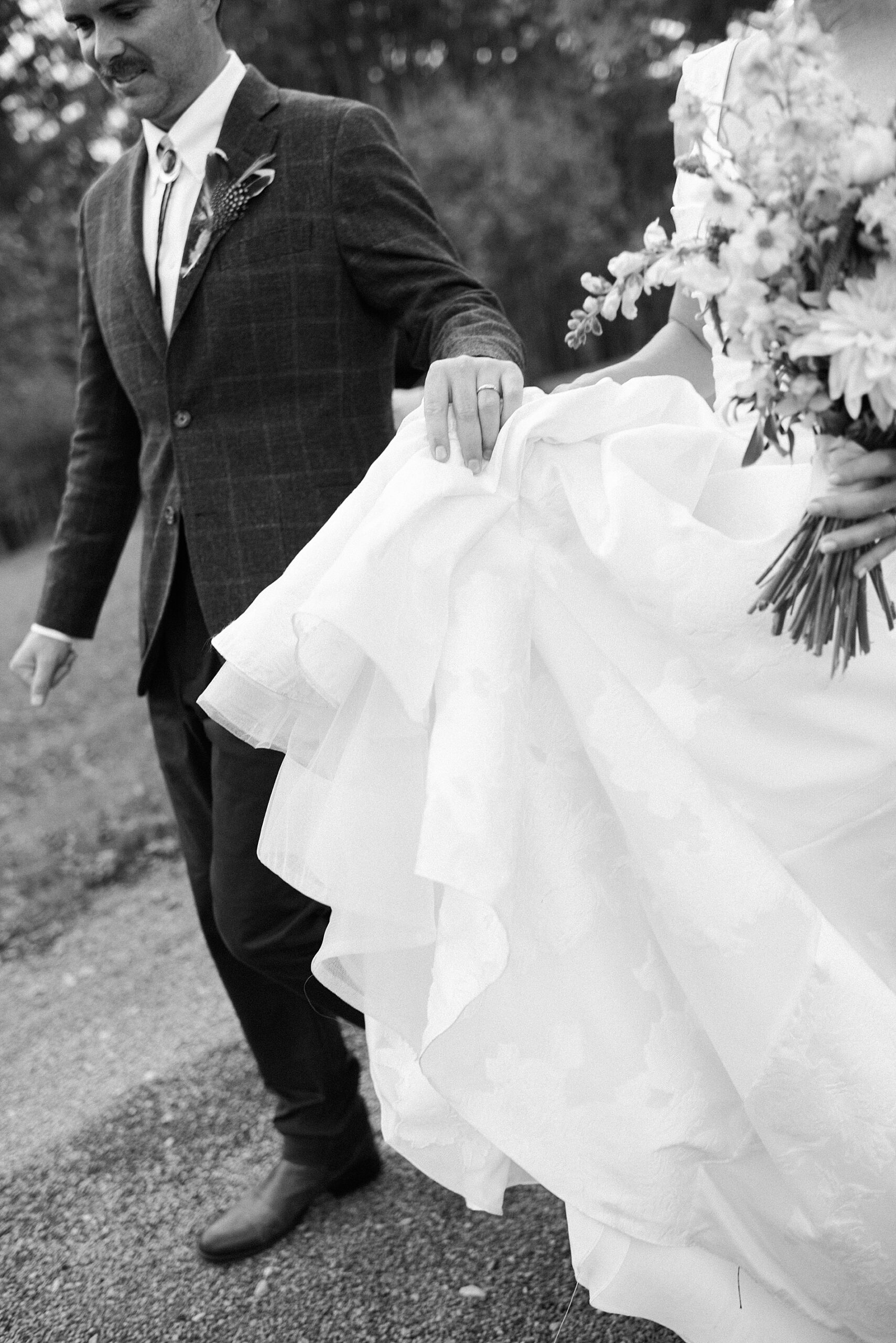 couple walk together while groom holds bride's wedding dress as they walk