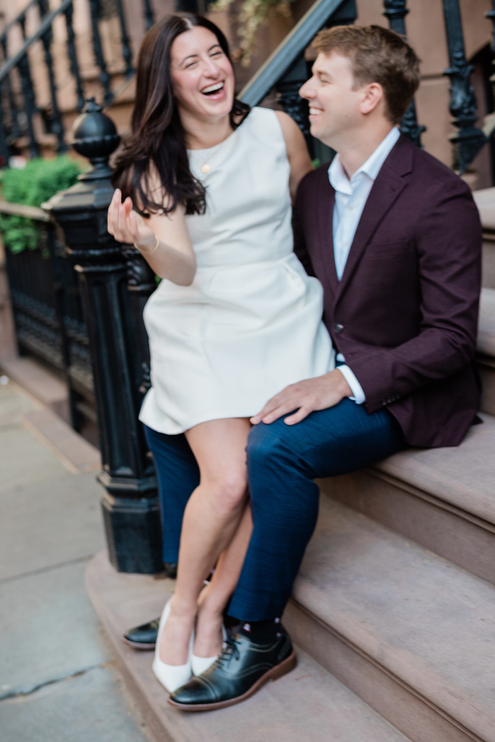joyful engagement photos of couple laughing as they sit together on stairs outside of building