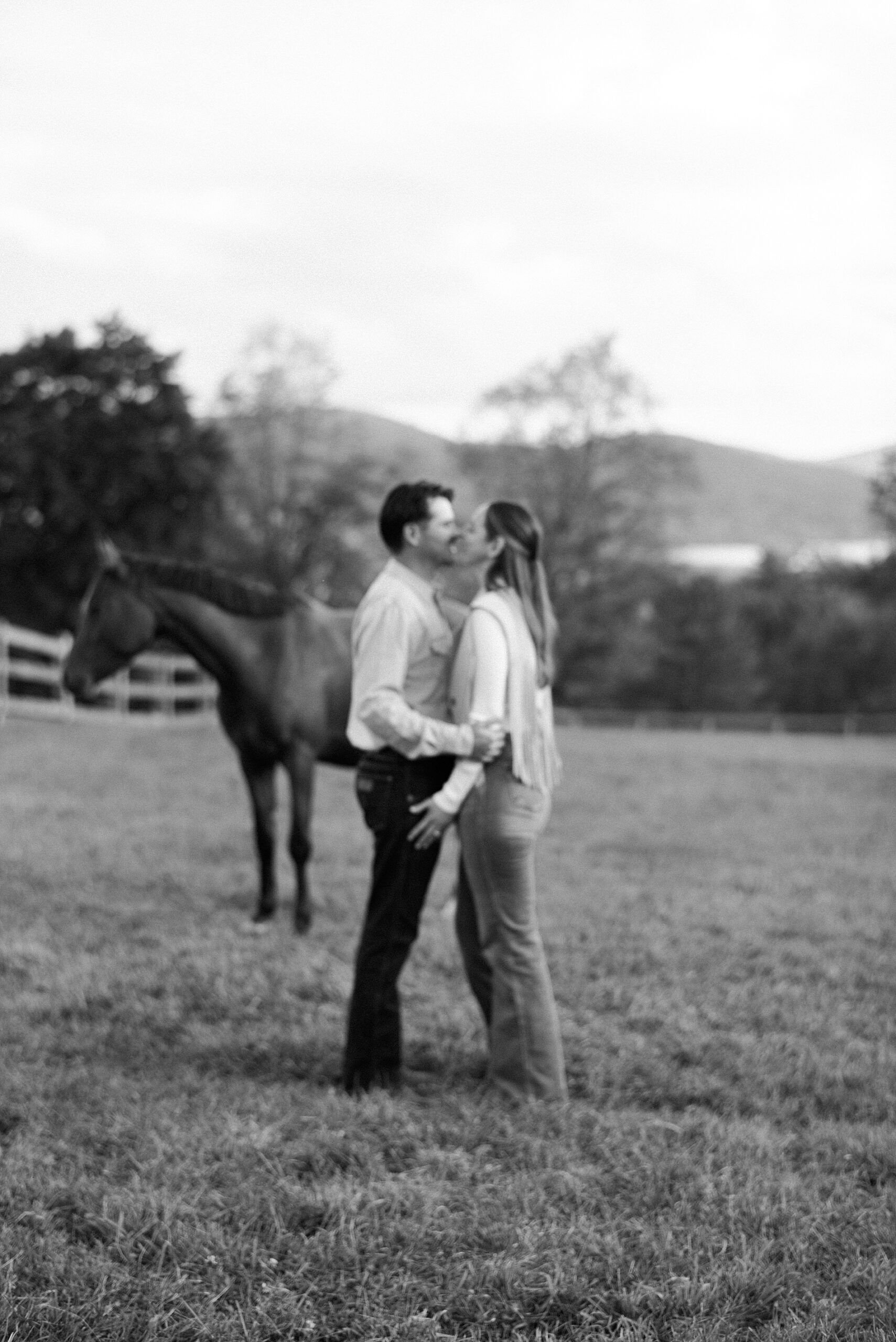 couple kiss in field with horse in the background 