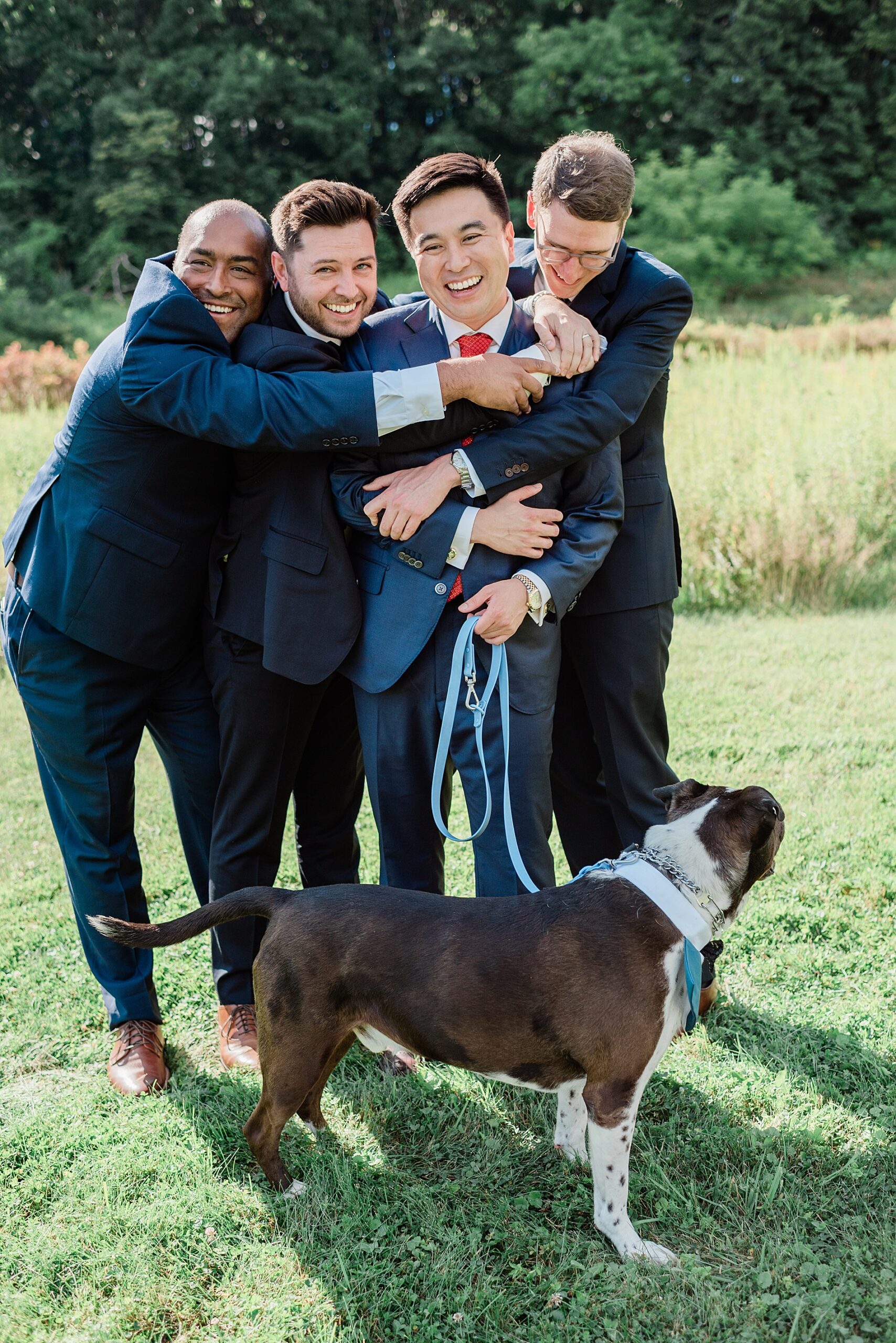 groomsmen hug groom who is holding dog's leash