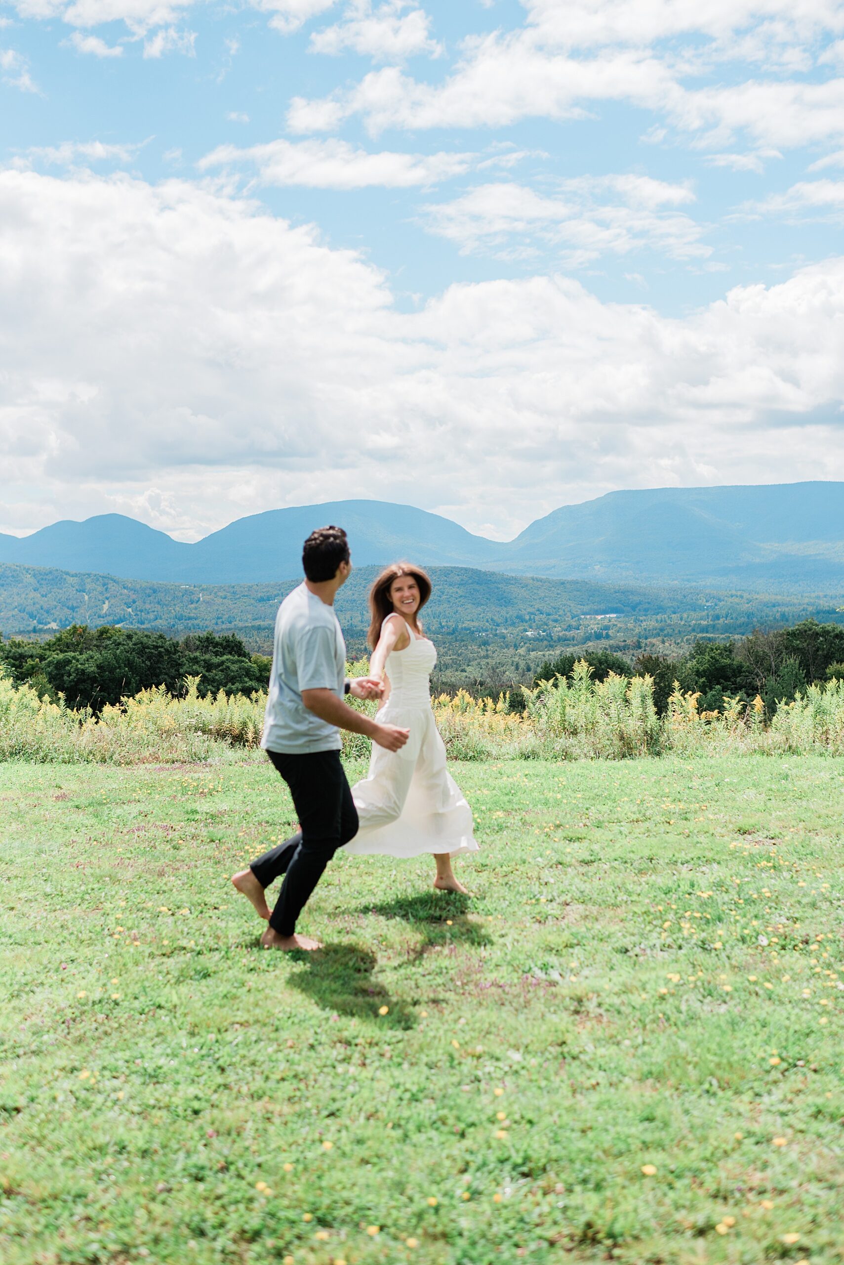 couple run together on hilltop with Catskills in the background 